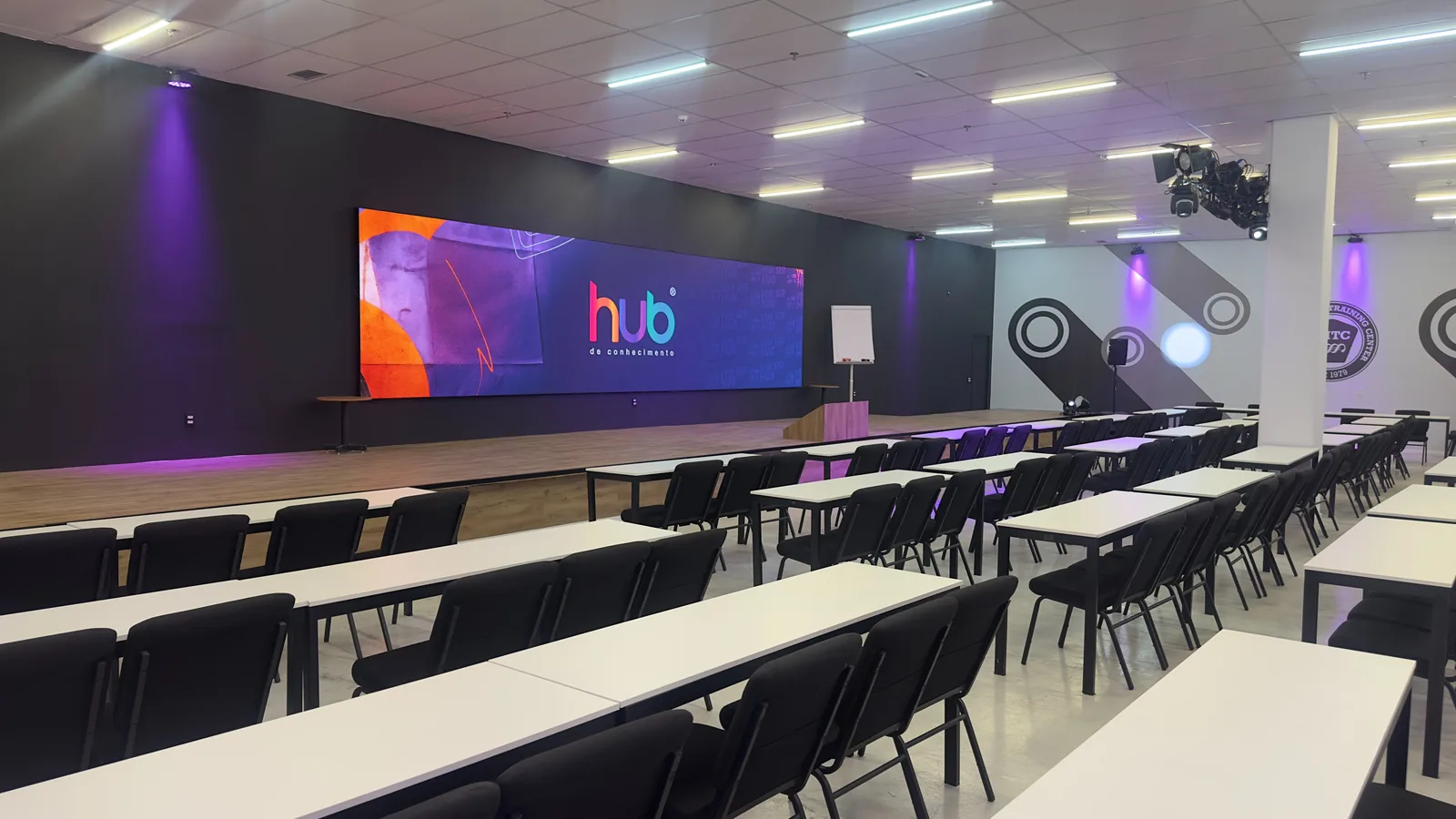 Vista lateral do auditório da HUB, com fileiras de mesas de trabalho voltadas para o palco